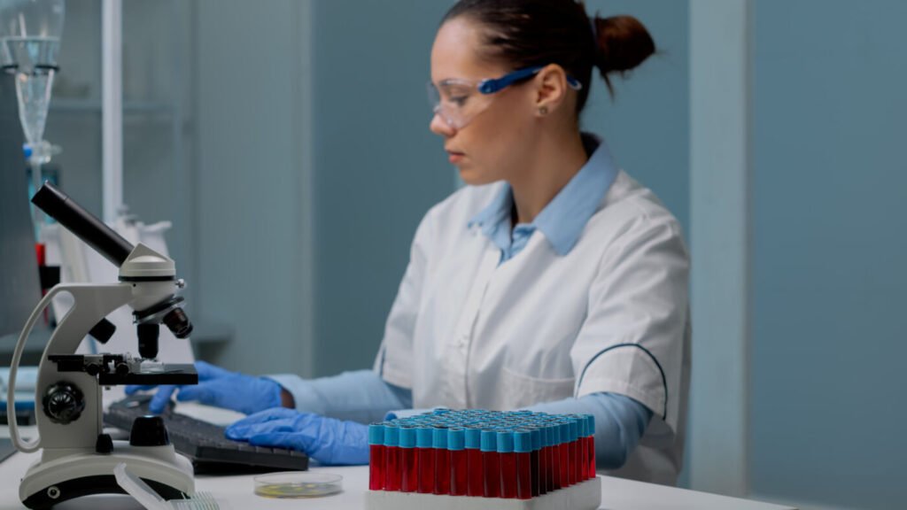 Laboratory specialist working at a computer beside sample tubes